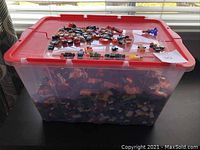 Red-lidded clear container filled with LEGO parts and minifigure pieces on top