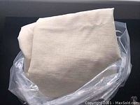 Ivory linen curtain panel folded and placed inside clear plastic wrapping, showing fabric texture and color.