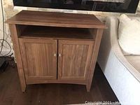 Front view showing wooden TV cabinet with two paneled doors and round metal knobs, open shelf, and visible wear on door finish and top surface.