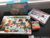 Lot of assorted games including LEGO Creationary, Don't Step In It, Snap Circuits Beginner electronic kit and a small puzzle cube in orange box.