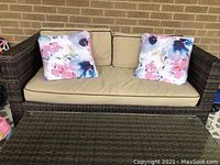 Front view of resin wicker sofa with beige cushions and two floral pillows