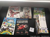 Photo showing 5 books including The Lego Play Book with a red Lego dragon on the cover, The Lego Builder's Guide with colorful scattered Lego bricks, Animal Atlas with Lego animal figures, The Lego Build-It Book: Amazing Vehicles with a red Lego truck, and a box set of 6 Lego Ideas Collection books.