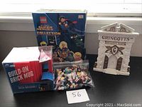 Photo showing the full lot: book, Build-on Brick Mug in box, Gringotts coin bank, and bag of mini dolls