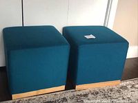 Two dark teal Threshold brand ottomans with wooden bases placed side by side on a carpet.