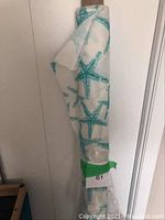 Roll of outdoor fabric with teal sea star pattern wrapped around a cardboard tube, labeled with green tape and tag '61'.