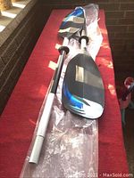 Full view of two-piece adult aluminum kayak paddle with black and blue accented blades, laid out on red surface.