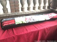 Carrying bag for Ventura Park and Beach Shelter, black with product label and shoulder strap, placed on red cloth.