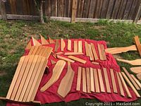 Overview of all wooden chair parts spread on red cloth outdoors on grass