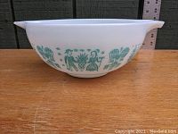 Side view of white glass mixing bowl with blue Amish Butterprint pattern showing figures and farm motifs