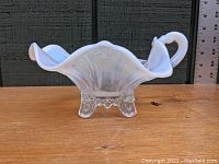 Front side view showing the ruffled top edge, handle, and clear pedestal legs of the white opalescent glass gravy boat.