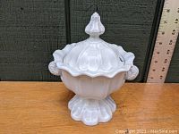 Front angle view of white ironstone sauce tureen with lid on wooden surface next to ruler for scale.