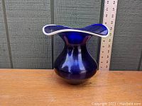 Side view of cobalt blue glass vase showing rounded body and flared white trimmed rim with a ruler for scale.