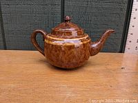 Side view of vintage redware teapot showing rounded body, handle, and spout with Rockingham glaze and decorative beige bands near the lid.