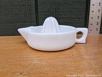 Side view of white opaque depression glass juice reamer showing handle and pouring spout with ruler background.