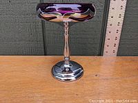 Side view of the amethyst glass compote bowl on chrome pedestal base against wood background with ruler for size reference