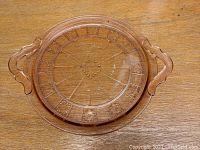 Top view of the round pink depression glass serving plate with handles, showing Doric patterned design.