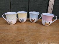 Four Lenox coffee cups with pastel bands and butterfly designs displayed side by side from the front