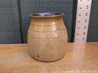 Front view of salt glazed stoneware crock showing incised text 'Millikin's Home Bakery 32 Waldon St' with ruler for scale.