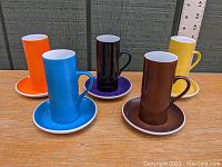 Five colorful demitasse cups and matching saucers arranged separately from front view on wooden surface