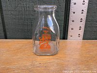 Front view of clear glass half pint milk bottle with orange lettering advertising 'Safe milk for the baby. Laboratory controlled'. Ruler shows approximately 4.5 inch height.