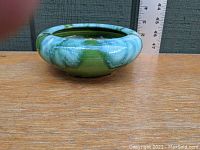 Photo of round low bowl planter showing green and white drip glaze with ruler for size reference.