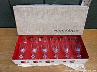 Six vintage Cristal d'Arques crystal champagne flutes in Rambouillet pattern arranged in original box with red interior and white textured lid with brand name.