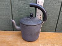 Side view of matte black tea kettle showing curved handle and spout with ruler in background for size reference.