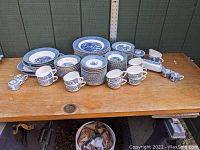 Photo overview of the Currier & Ives Royal China dinnerware arranged on a wooden table showing plates, cups, saucers, salt and pepper shakers, and serving pieces.