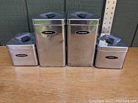 Front view of four chrome Masterware kitchen canisters labeled flour, sugar, coffee, and tea.