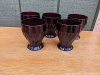 Front side view of the five ruby red swirl tumblers arranged in a line on a wooden surface.