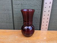 Side view of royal ruby depression glass vase showing shape, color, and size relative to ruler.