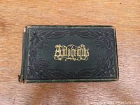 Photo of closed autograph book with embossed green cover and gold title "Autographs."