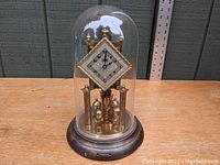 Full view of the clock under original glass dome on brass base with visible wear.