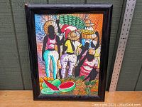 Painting framed in black wood, showing five faceless figures in a Jamaican market setting with pineapples and watermelons. The frame shows some veneer damage on edges.
