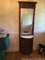 Front view of the hall tree showing the wooden frame, etched mirror, and stone tabletop with hooks on sides.