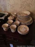 Full view of the Mikasa Heritage china set including stacked dinner plates, bowls, cups, saucers, creamer, and sugar bowl with floral motif on an ivory base, arranged on dark wooden surface.