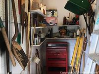 Shelf and wall corner showing long handled gardening tools including shovels, rakes, hand saws, small hand tools on shelves