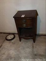 Full view of the wooden table showing one drawer, open shelf, and surrounding floor with wall background.