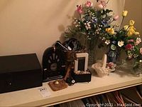 Wide shot of shelf including flowers, box, radio, and bathroom decor