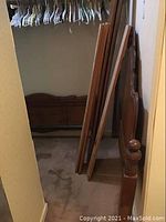 View of unassembled wooden headboard, footboard, and side rails leaning against a wall in a closet space.