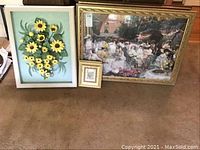 Photo showing 7 pieces of wall art arranged on floor including large floral 3D piece, large impressionist garden party print with gold frame, and smaller framed art pieces.