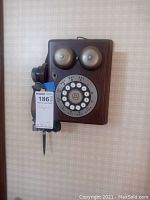 Front view of vintage wall-mounted rotary dial telephone showing wooden body, two metal bells, rotary dial and wooden receiver with chips.