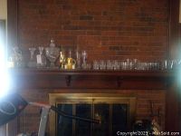Wide view of mantel showing the collection of decanters and glassware including a ceramic decanter and various clear glass decanters, glasses, and Crown Royal holders.