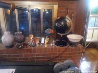 Photo showing all items on brick ledge including globe, dog figurines, hot air balloon figurine, ginger jar, bowl, and wall hooks in the background.