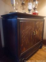 Front view showing painted landscape motif on cabinet doors and brass hardware