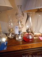 Four glass oil lamps on wooden surface, varying in base design and size, wide view of lot
