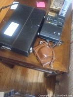 Photo showing Kodak Colorburst 250 camera, brown leather camera case, and black camera case on wood table.