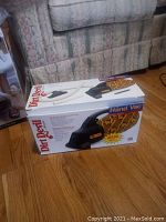 Boxed Dirt Devil handheld vacuum cleaner with hose and vacuum attachment, placed on wooden floor in front of sofa.