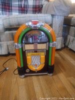 Front view of the Crossley tabletop jukebox showing the curved top, colorful orange and green plastic trim with silver chrome accents, and song selection panel.