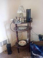 Three-shelf wooden table in corner against wall with some items on it (not included). Table has turned legs and circular shelves.